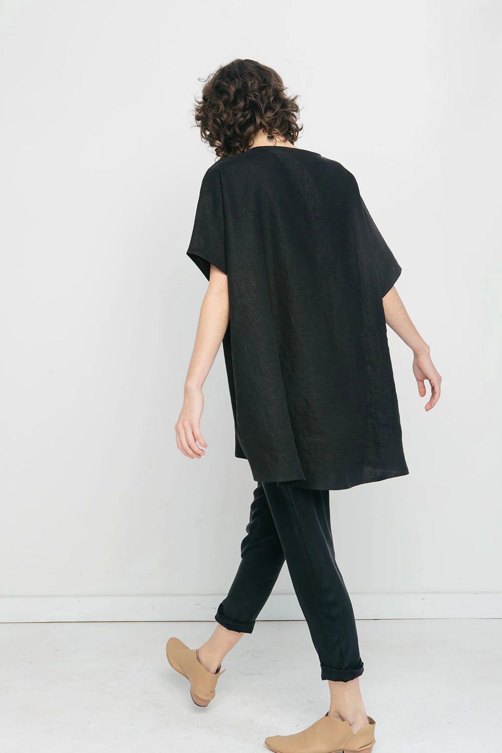 Person wearing a black oversized tunic and black pants against a white background