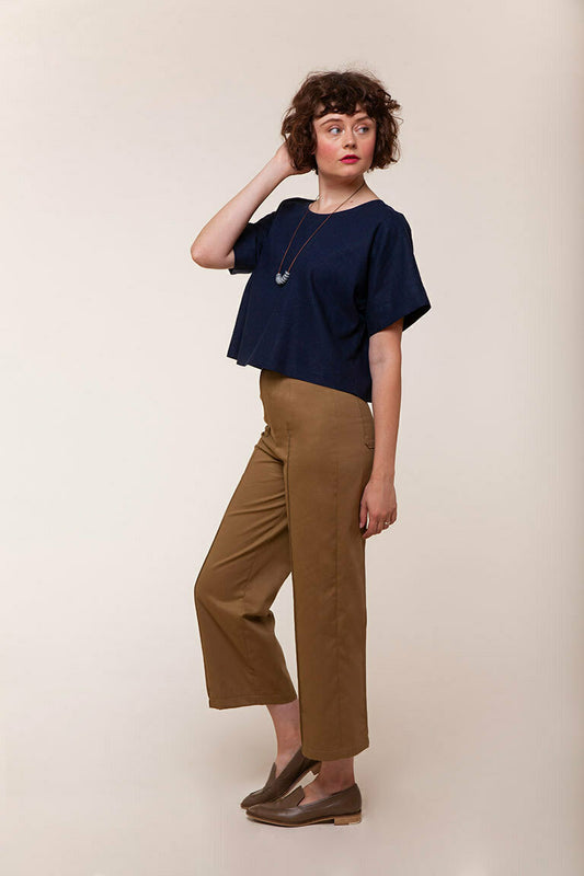 Woman wearing a navy top and brown pants against a beige background