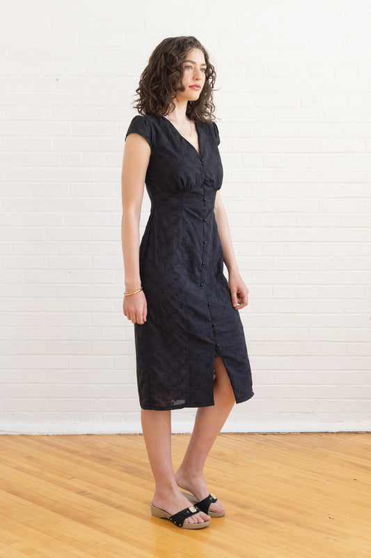 Woman wearing a black dress standing against a white wall.