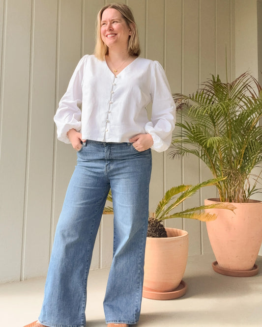 Woman wearing a white blouse and blue jeans standing in front of potted plants.