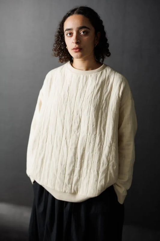 Person wearing a cream cable knit sweater against a dark background