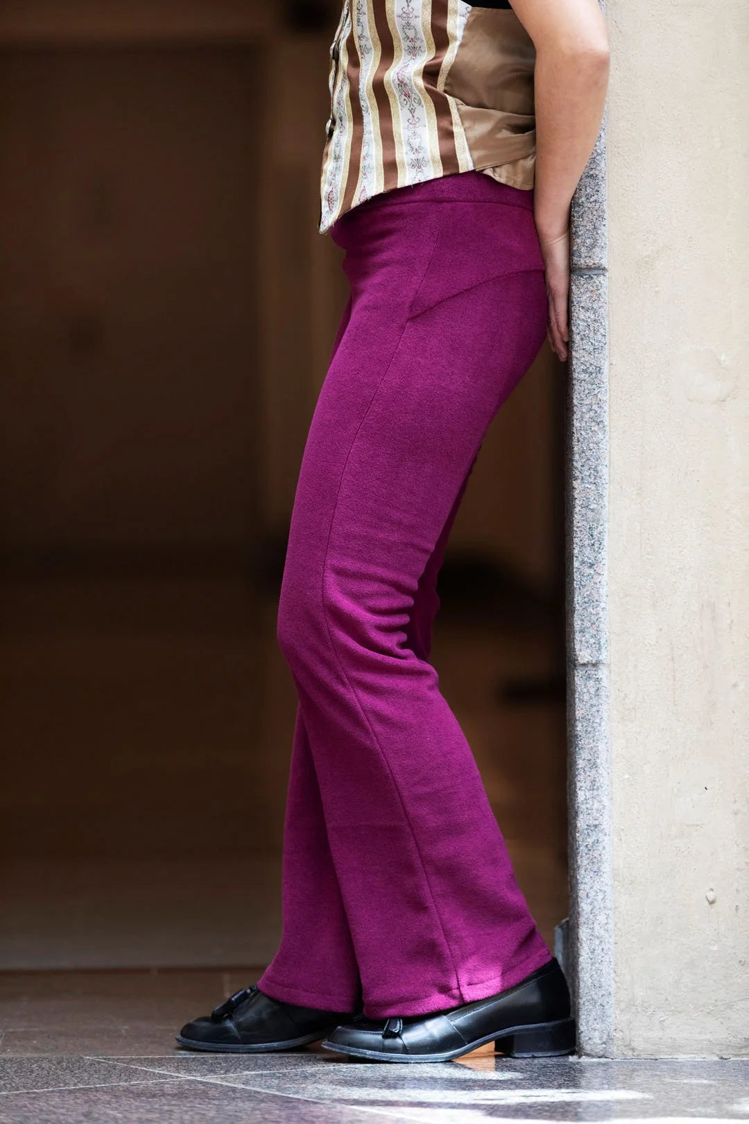 Person wearing magenta flared pants and a striped shirt, standing against a neutral wall.