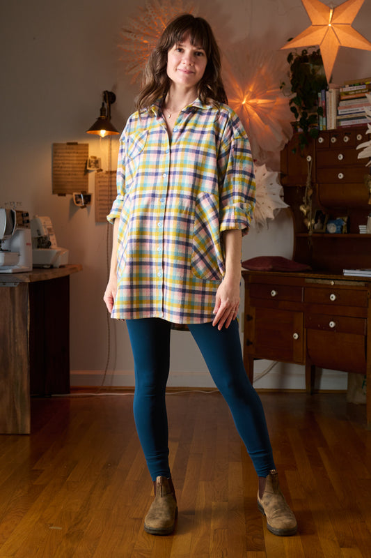 Woman wearing a plaid shirt and blue leggings standing in a room with wooden floors and furniture.