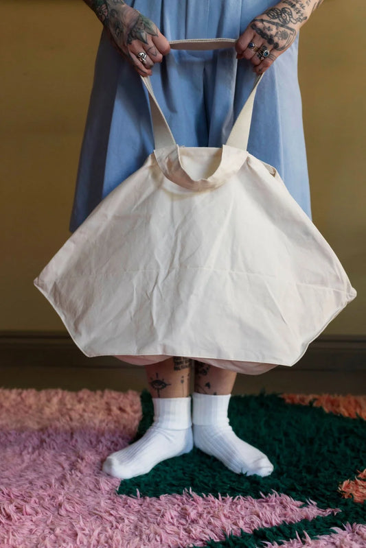 Person holding a white tote bag on a textured pink and green rug.