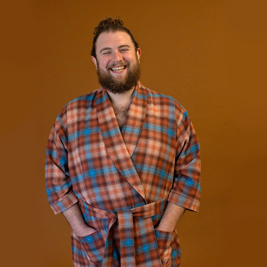 A person standing and smiling, wearing a plaid Arbutus Robe with a shawl collar and pockets.