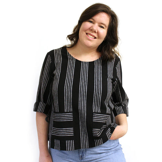 A woman wearing a long sleeved black and white striped top with three quarter, cuffed sleeves.