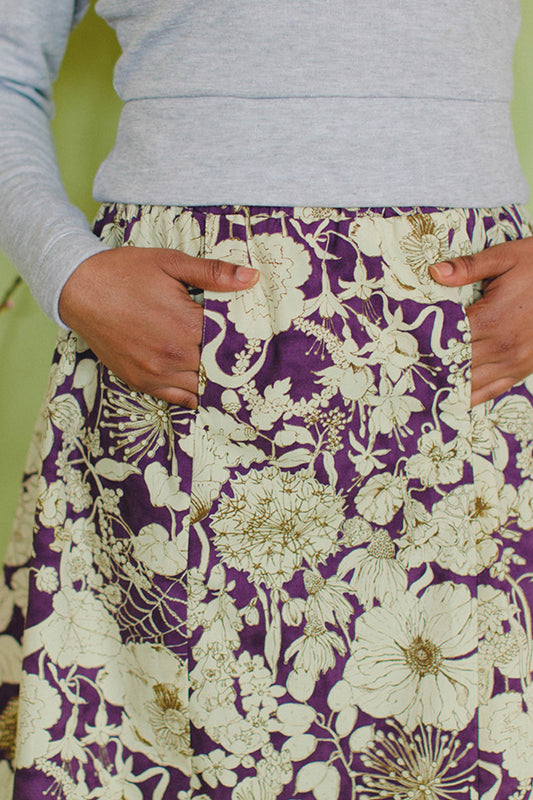 close detail of a woman with her hands in the pockets of midi skirt in a cream and purple floral print