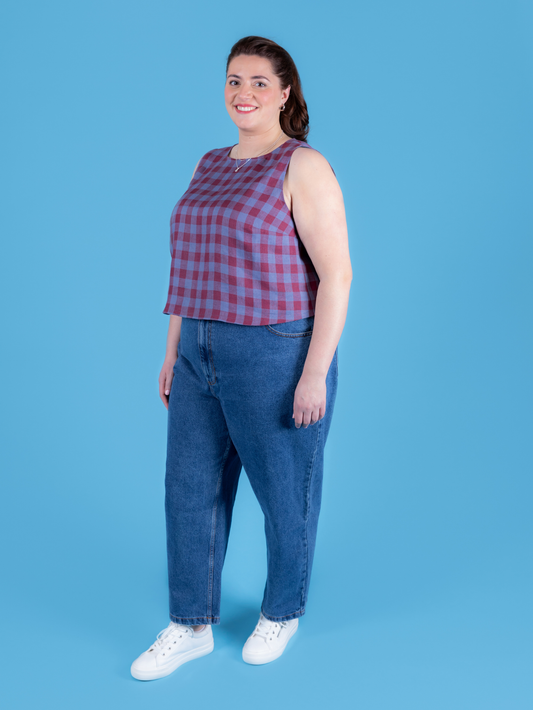 Woman wearing a red and purple checkered top and blue jeans against a blue background