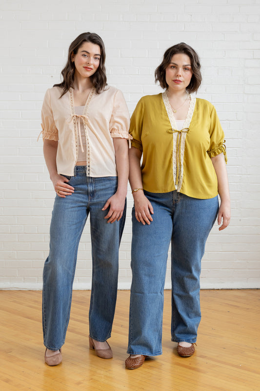 Two women wearing matching outfits with beige tops and blue jeans on a plain background