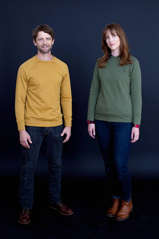 Two people wearing mustard yellow and green sweaters against a dark background