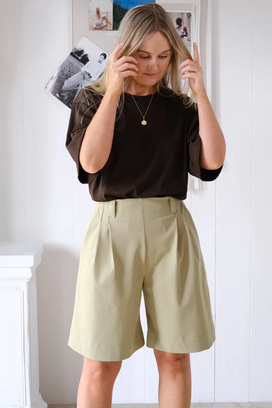 Woman wearing a black top and beige shorts indoors.