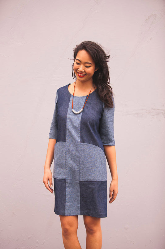 Woman wearing a blue patchwork dress against a plain background