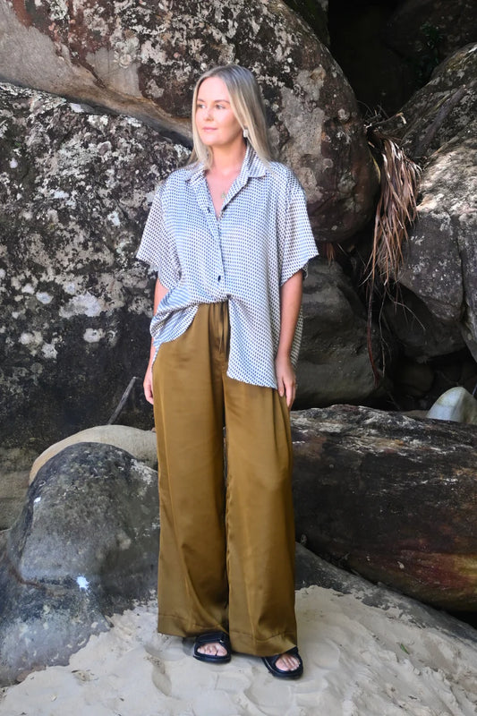 Woman standing on a rocky beach wearing a blue and white checkered shirt and brown pants.