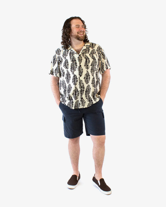 Man wearing a patterned shirt and navy shorts on a white background