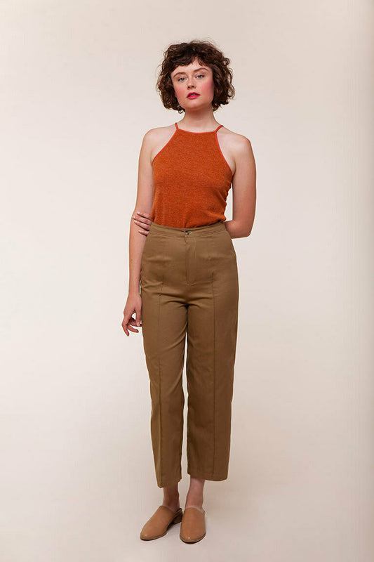 Woman wearing a rust-colored halter top and brown pants against a beige background