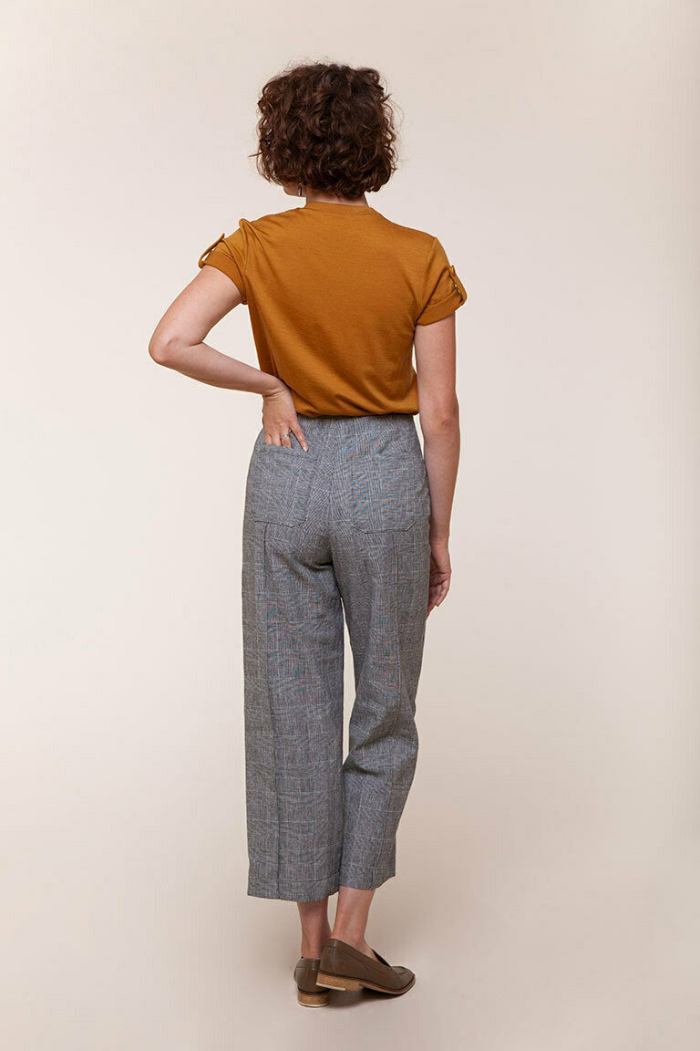 Person wearing a mustard yellow top and gray checkered pants on a beige background