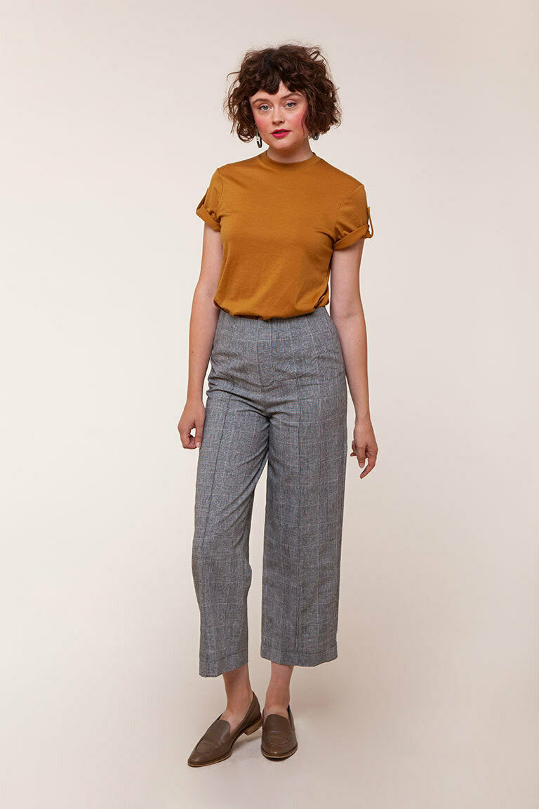 Woman wearing a mustard yellow top and gray checkered pants on a white background