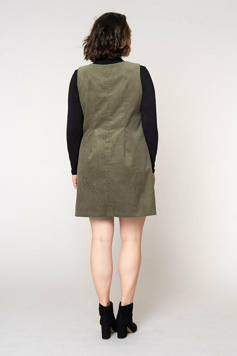 Person wearing a green corduroy dress over a black long-sleeve shirt on a white background
