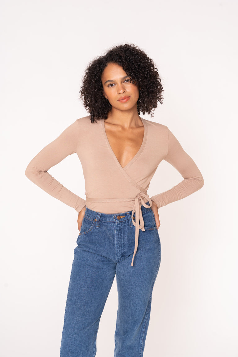 Woman wearing a beige wrap top and blue jeans on a white background