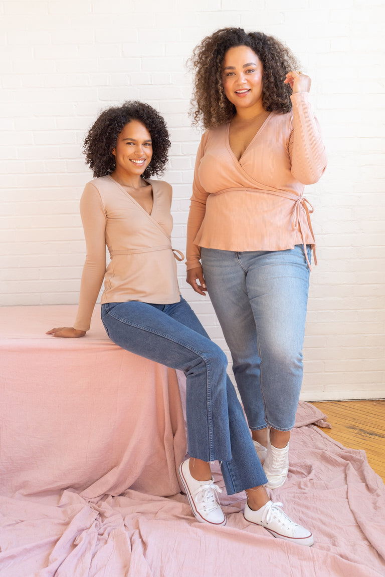Two women posing together on a pink blanket against a white wall.
