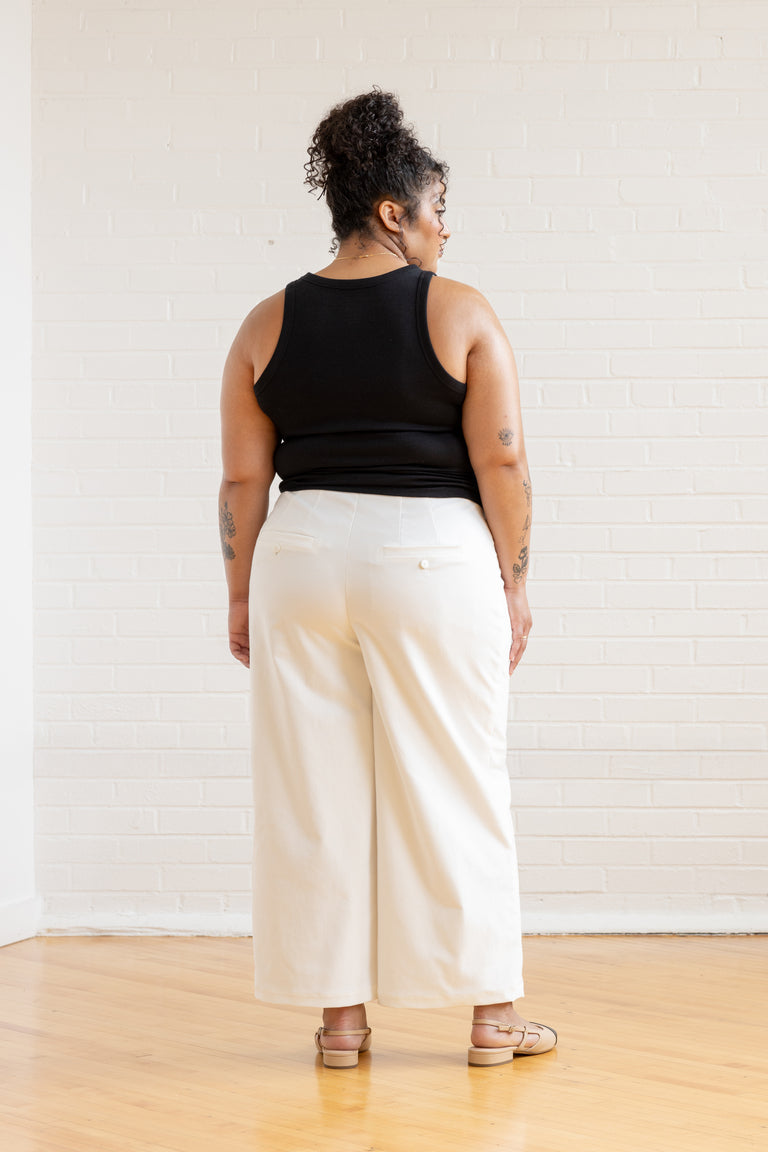 Person wearing a black sleeveless top and white pants against a plain background