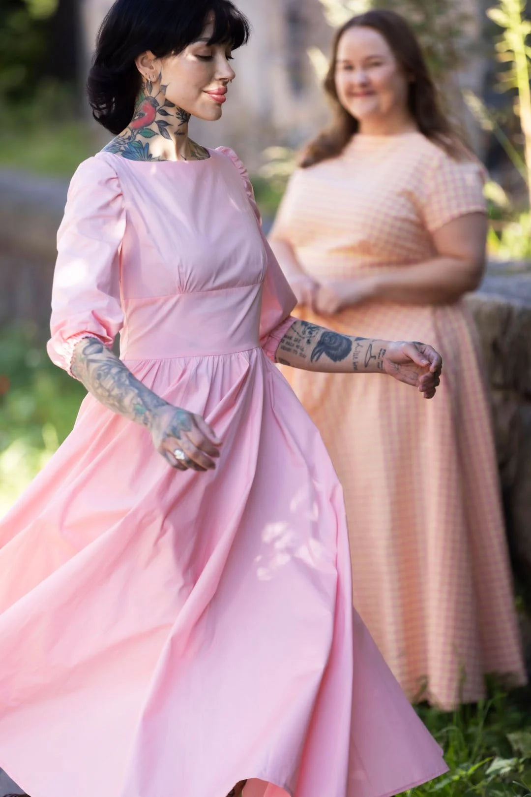 Two women in pink dresses standing outdoors with a blurred background