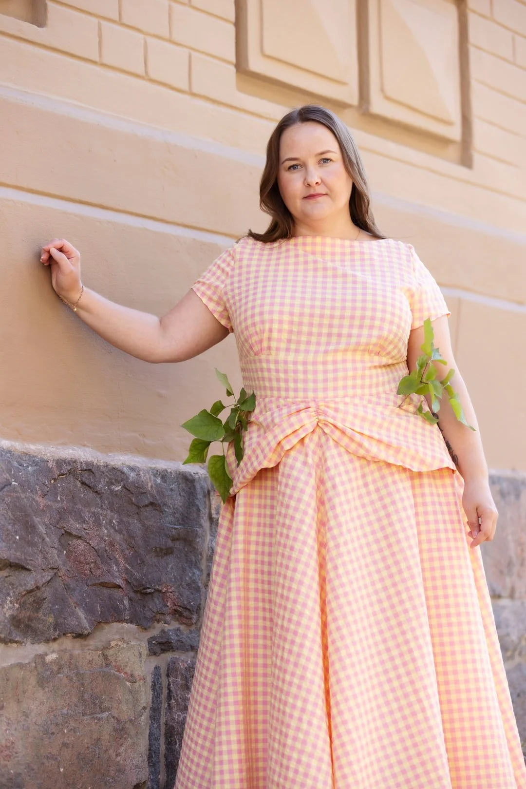 Woman in a peach checkered dress standing against a beige wall.