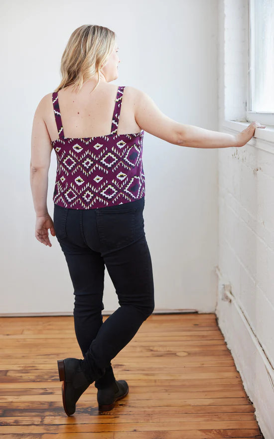 Woman wearing a patterned top and black pants standing in a room with wooden flooring.