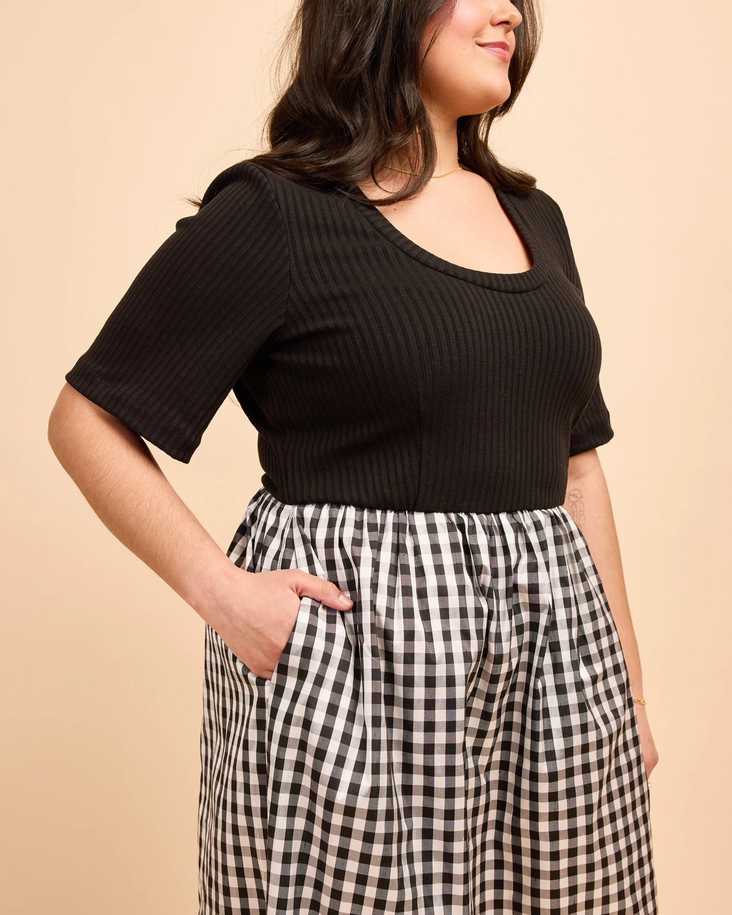 Woman wearing a black ribbed top and checkered pants against a beige background