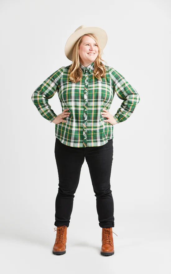 Person wearing a green plaid shirt, black pants, brown boots, and a beige hat on a white background