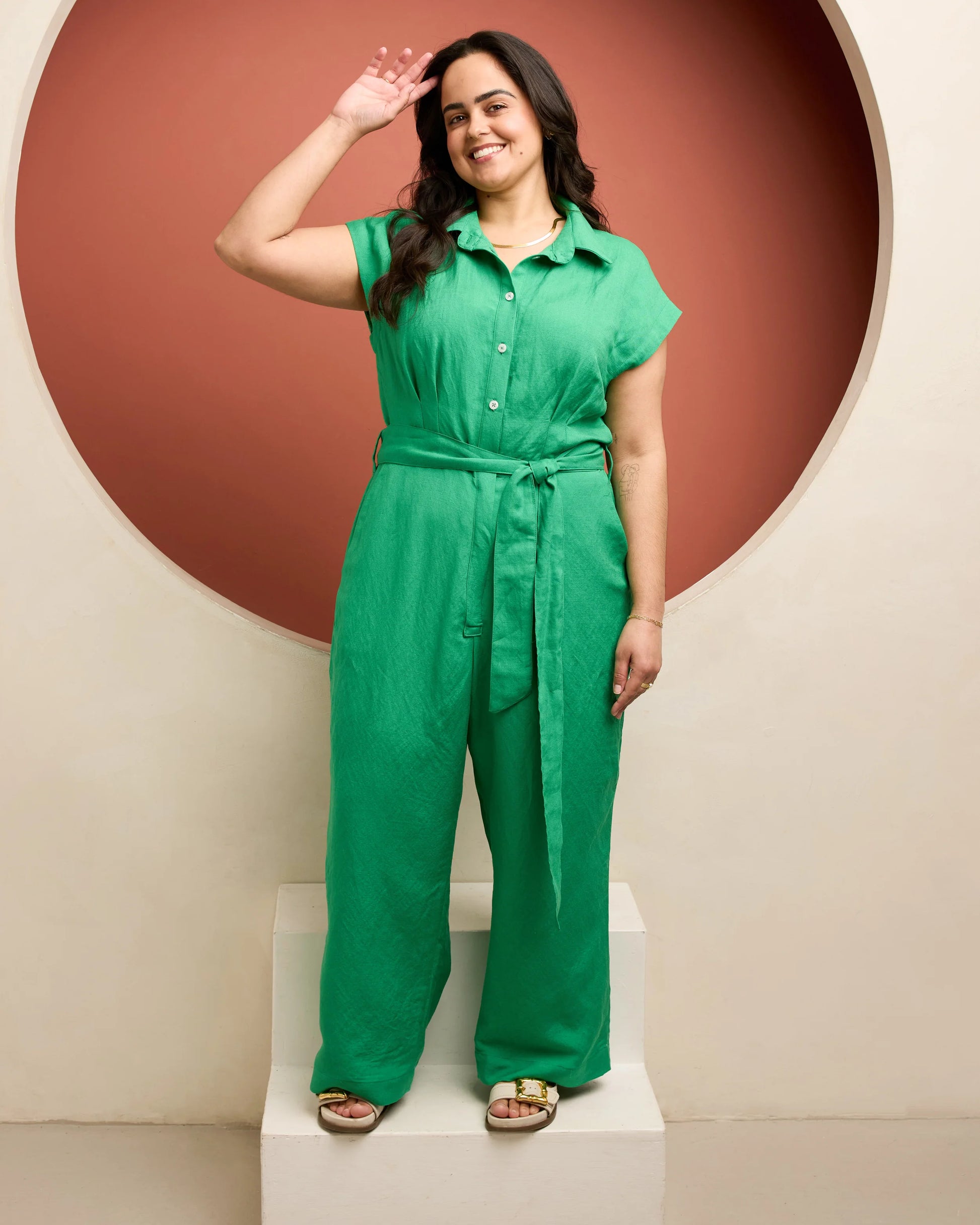 Woman wearing a green jumpsuit standing against a red and beige wall.