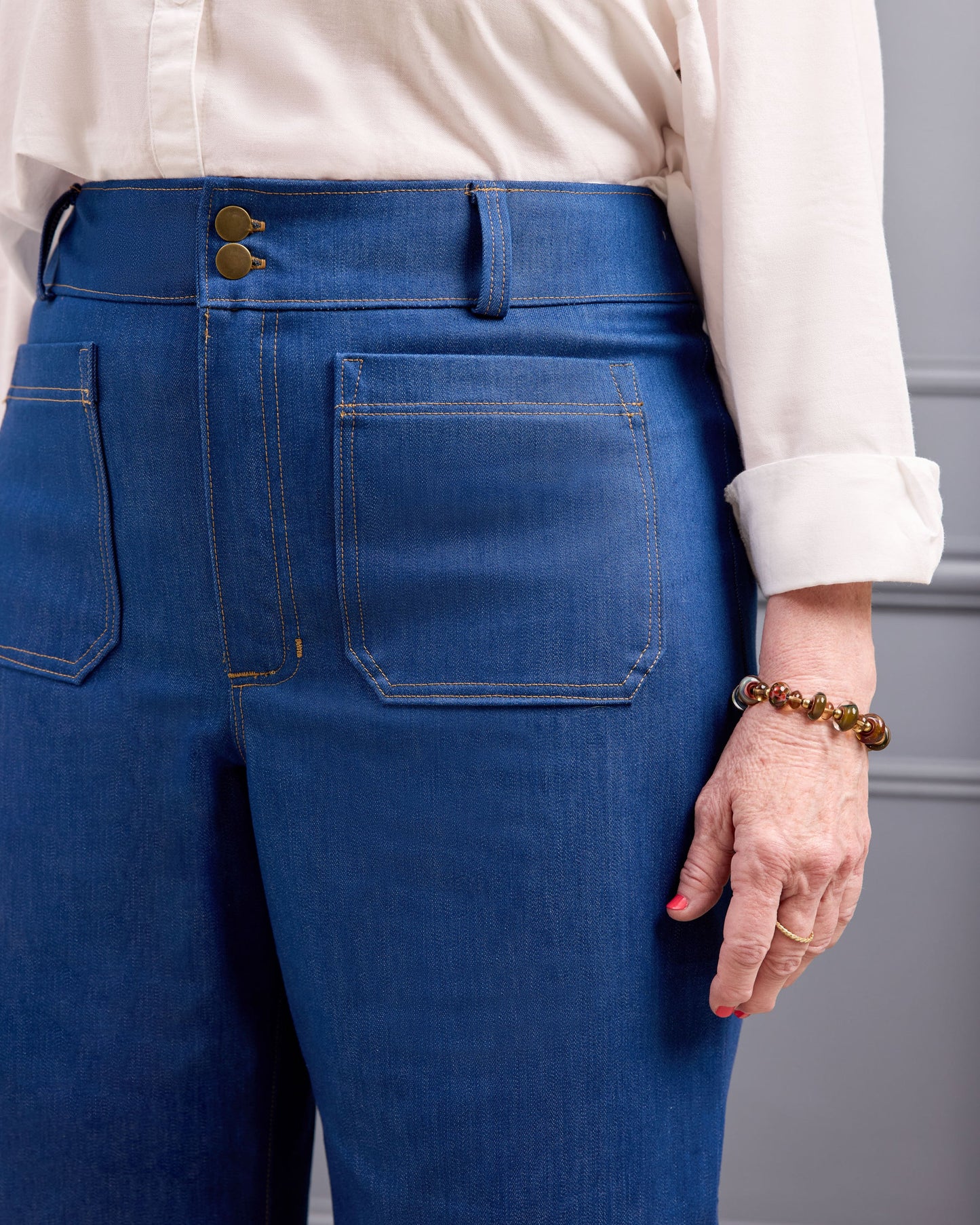 Close-up back view of a person wearing blue denim jeans with a cream blouse, showing the waistband, button closure, and back pockets.