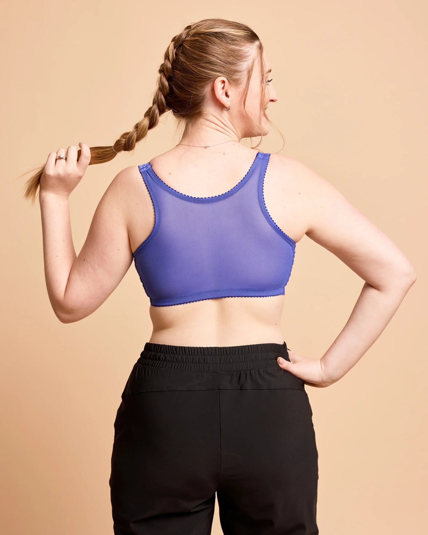 Woman wearing a purple sports bra and black leggings against a beige background