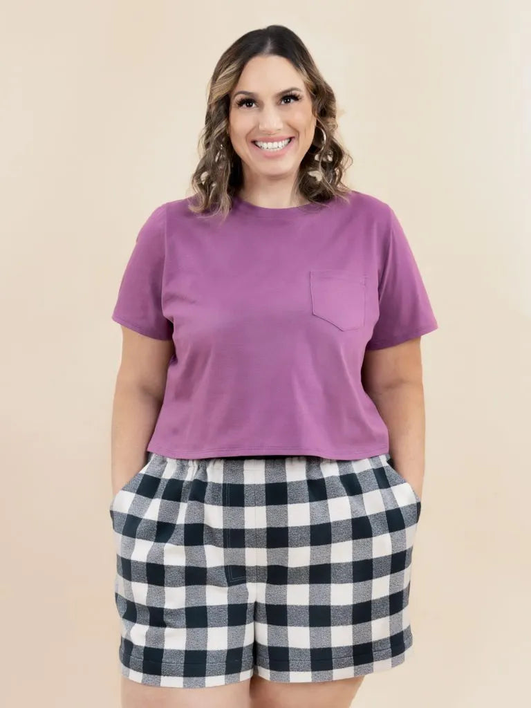 Woman wearing a purple t-shirt and plaid shorts on a beige background
