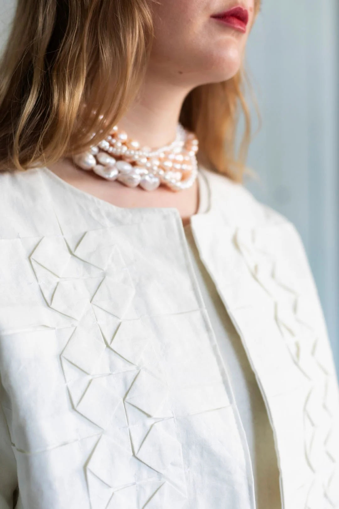 Close-up of a person wearing a white textured jacket and pearl necklace.