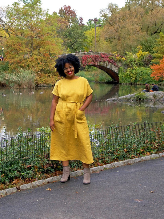 Woman in a yellow dress standing in a park with a lake and bridge in the background