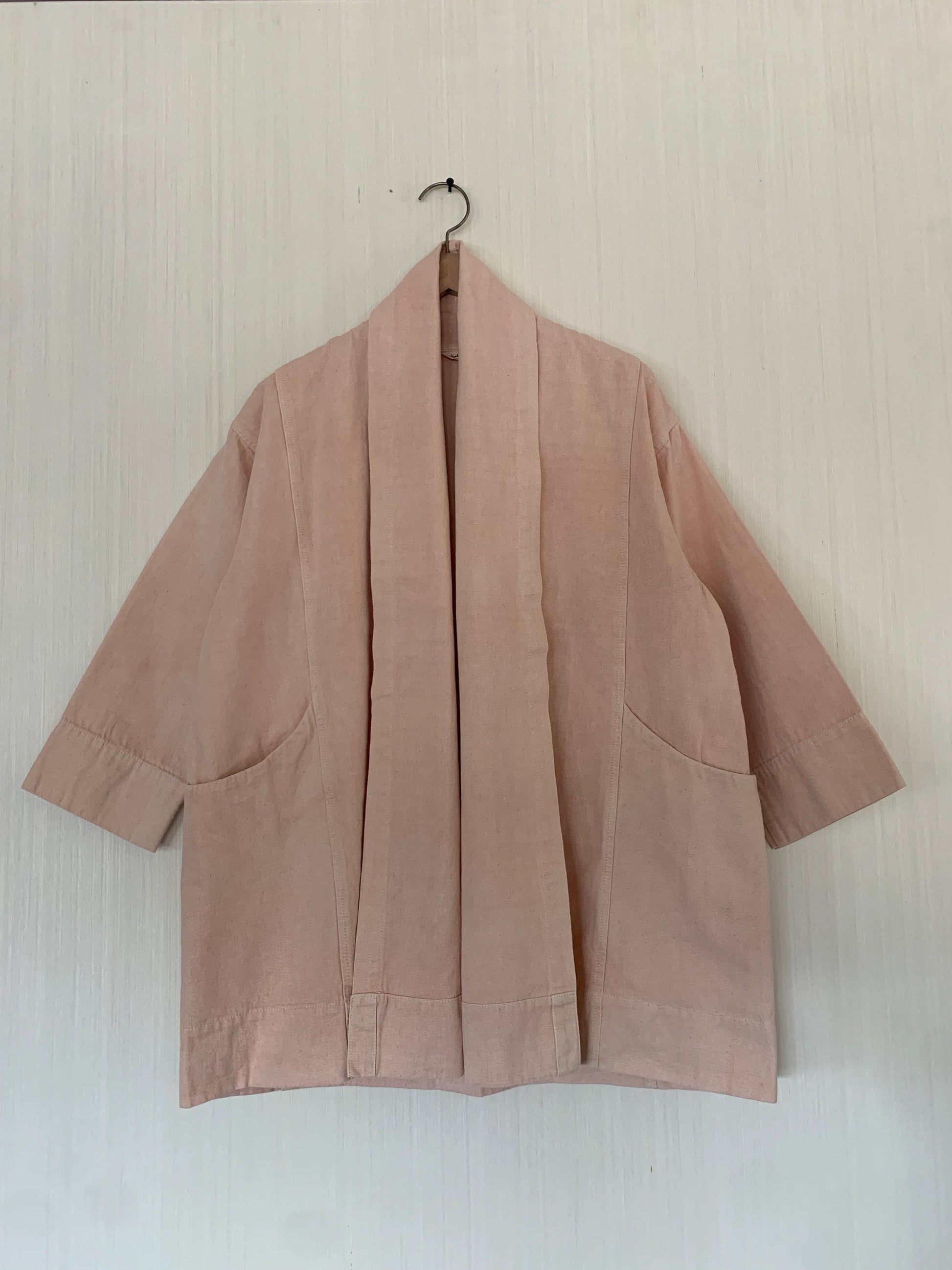 Pink kimono-style garment hanging on a hook against a light background
