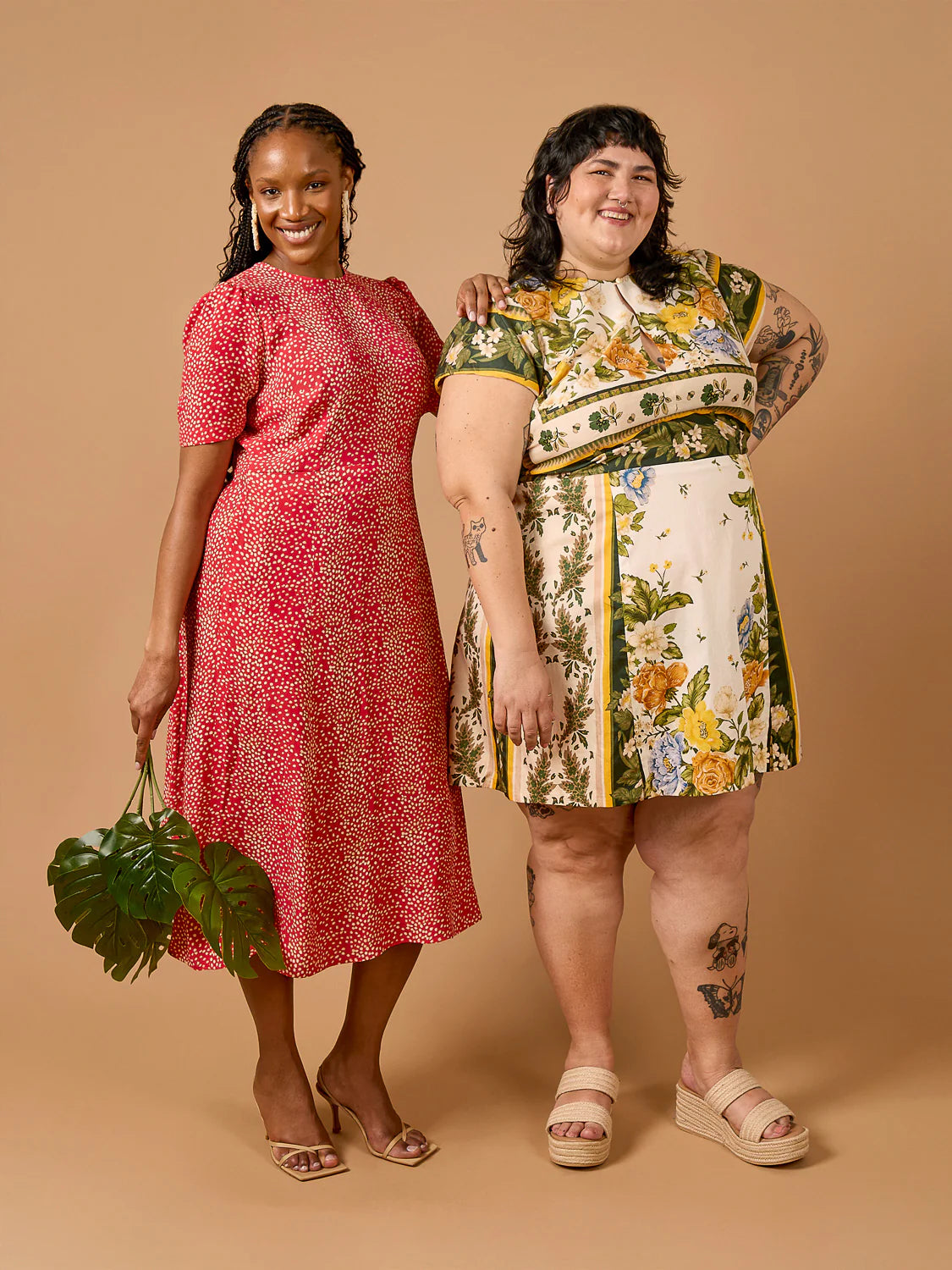 Two women wearing patterned dresses standing against a beige background