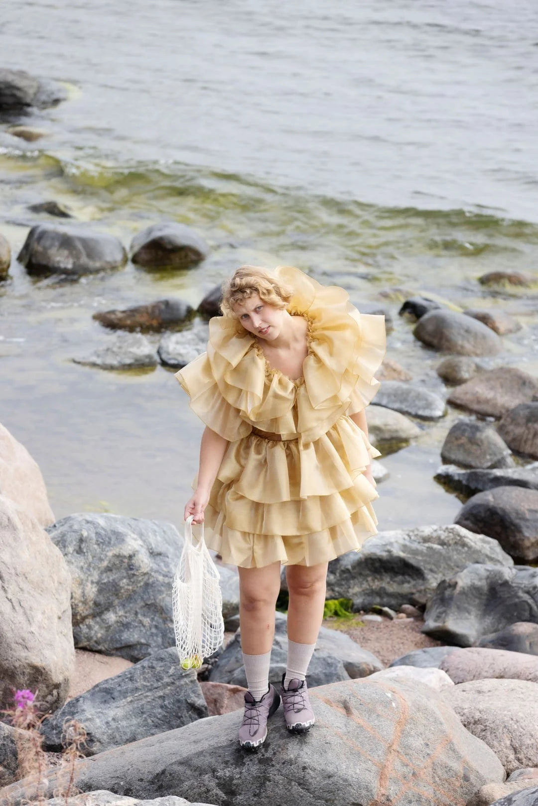 Person in a yellow dress standing on rocks by a body of water