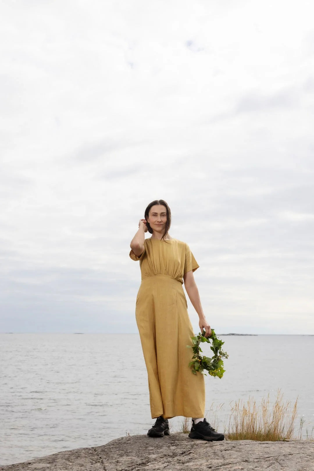 Woman in a yellow dress holding a wreath against a cloudy sky.