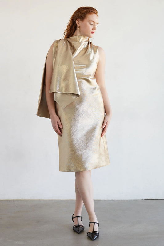 Woman wearing a gold dress with a cape against a white background