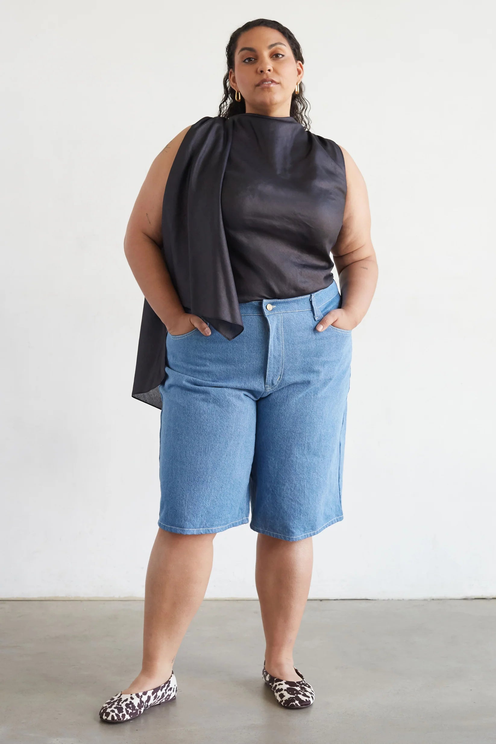 Woman wearing a black sleeveless top and blue shorts against a white background