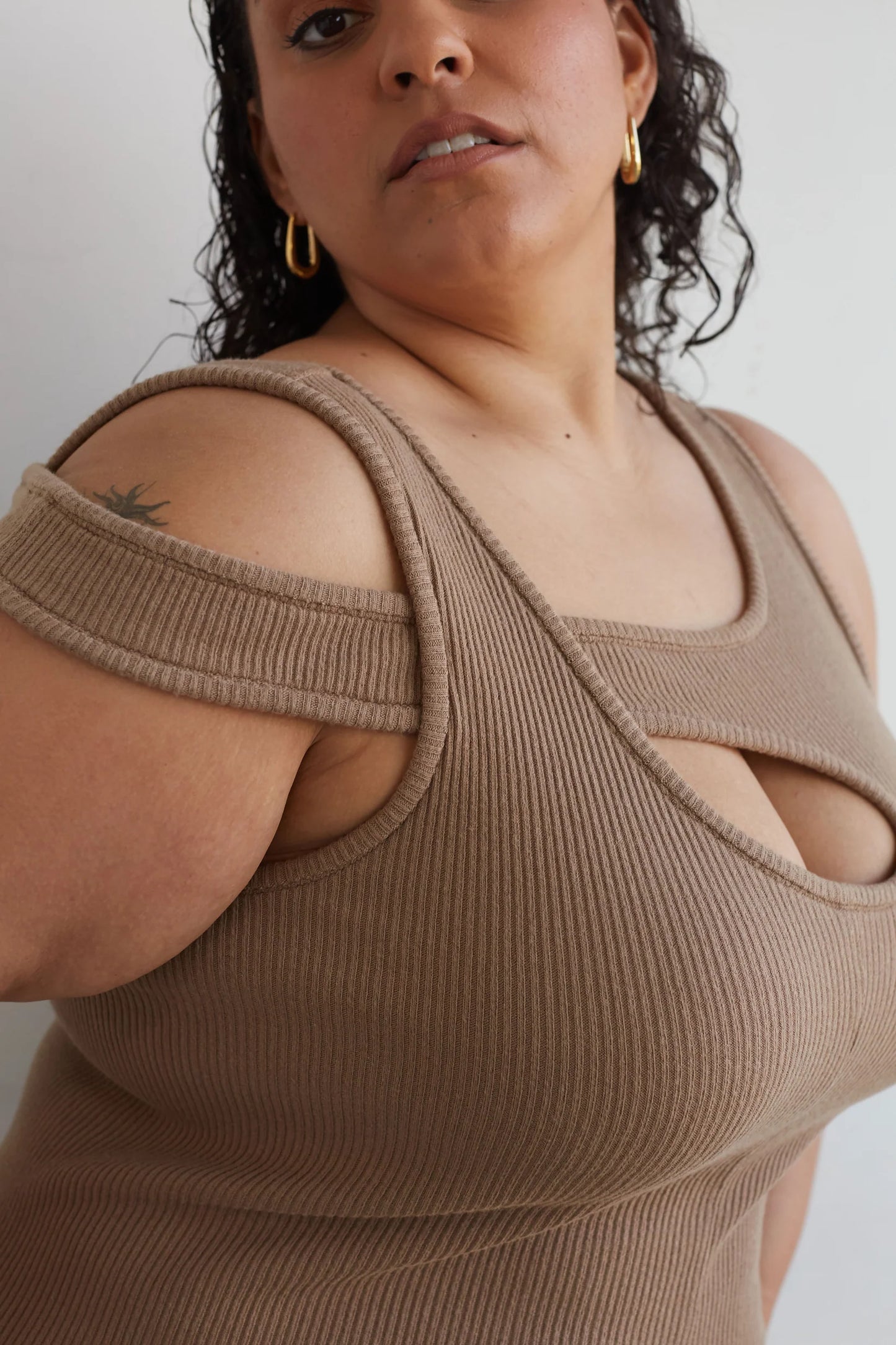 Woman wearing a beige ribbed tank top with cut-out design on a plain background