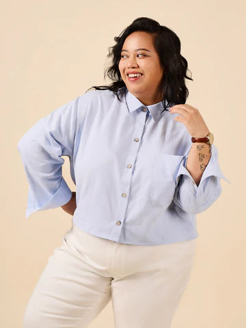 Woman wearing a light blue button-up shirt and white pants on a beige background