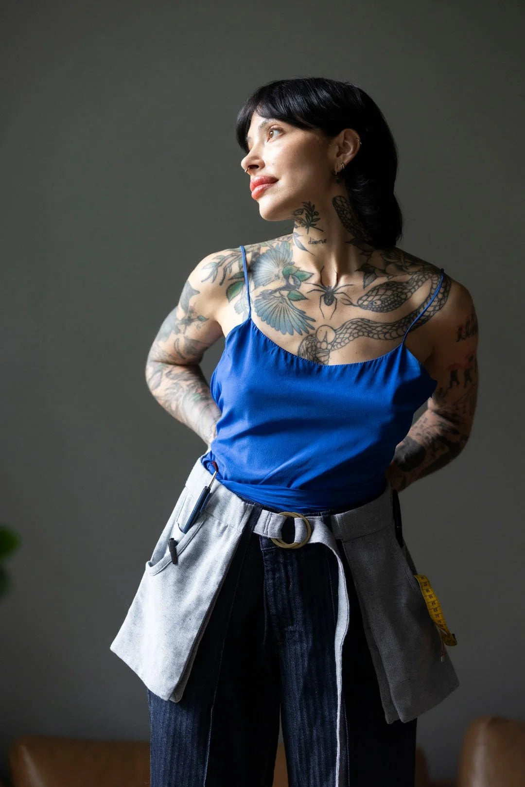 Woman with tattoos wearing a blue top and apron against a plain background