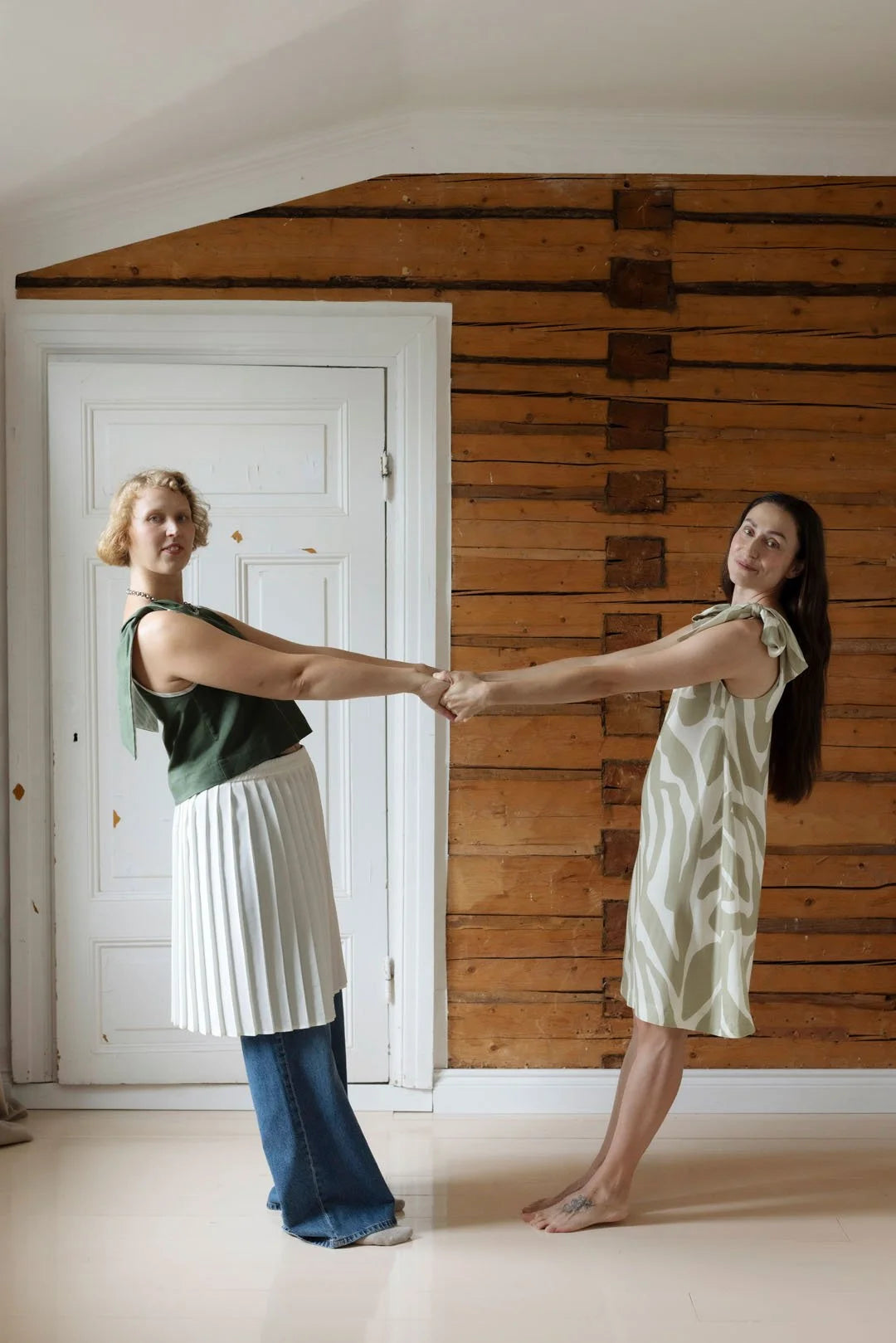 Two women holding hands against a wooden paneled wall.
