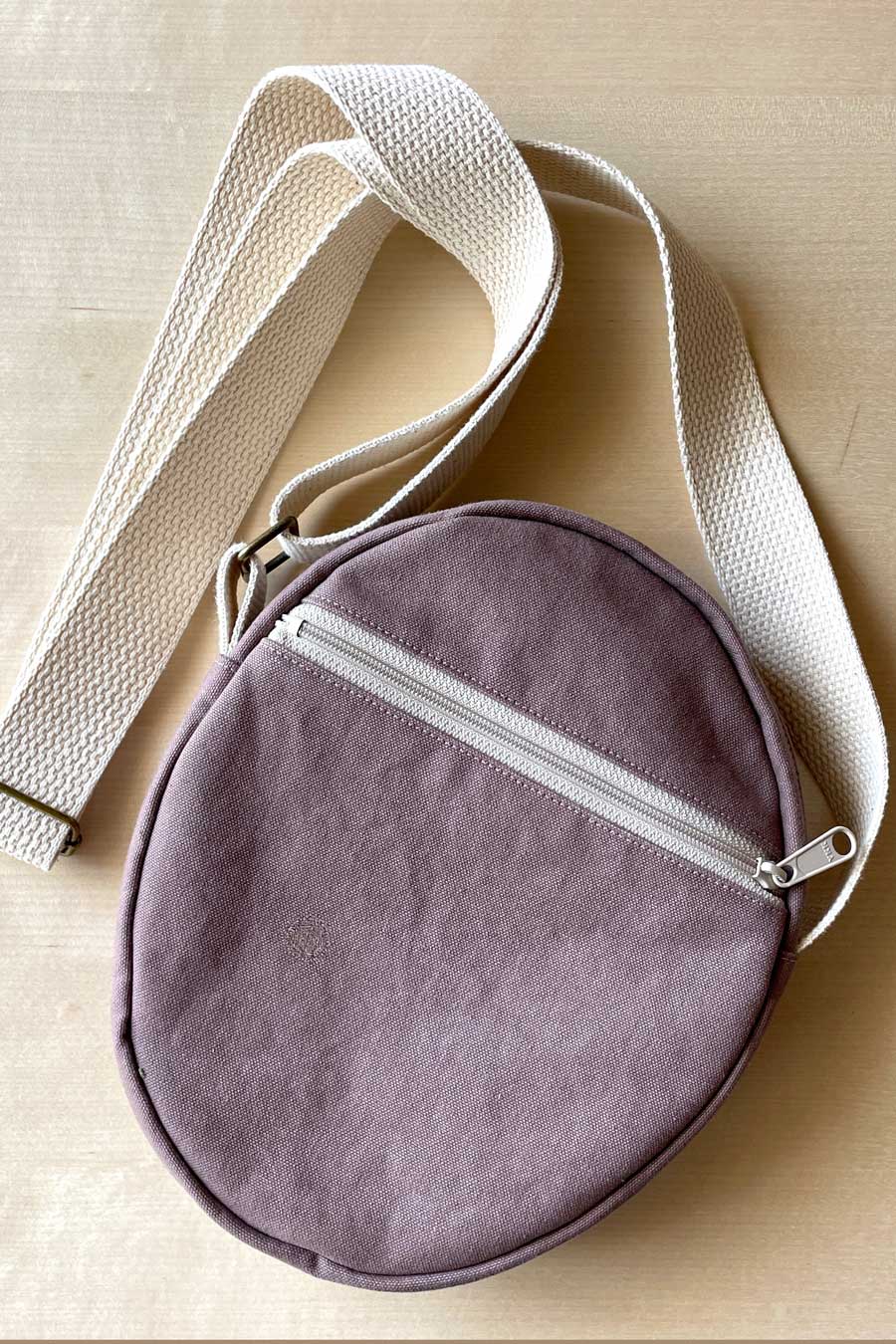 Round purple bag with a beige strap on a light wooden surface