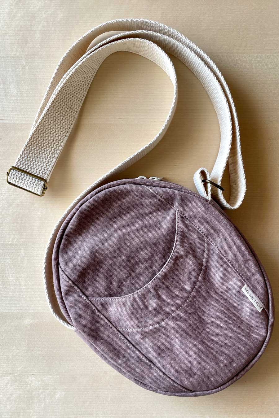 Purple crossbody bag with a strap on a beige surface