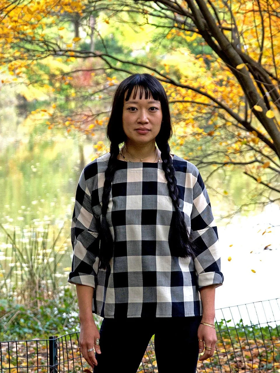 Person wearing a black and white checkered shirt in an outdoor setting with trees and foliage.