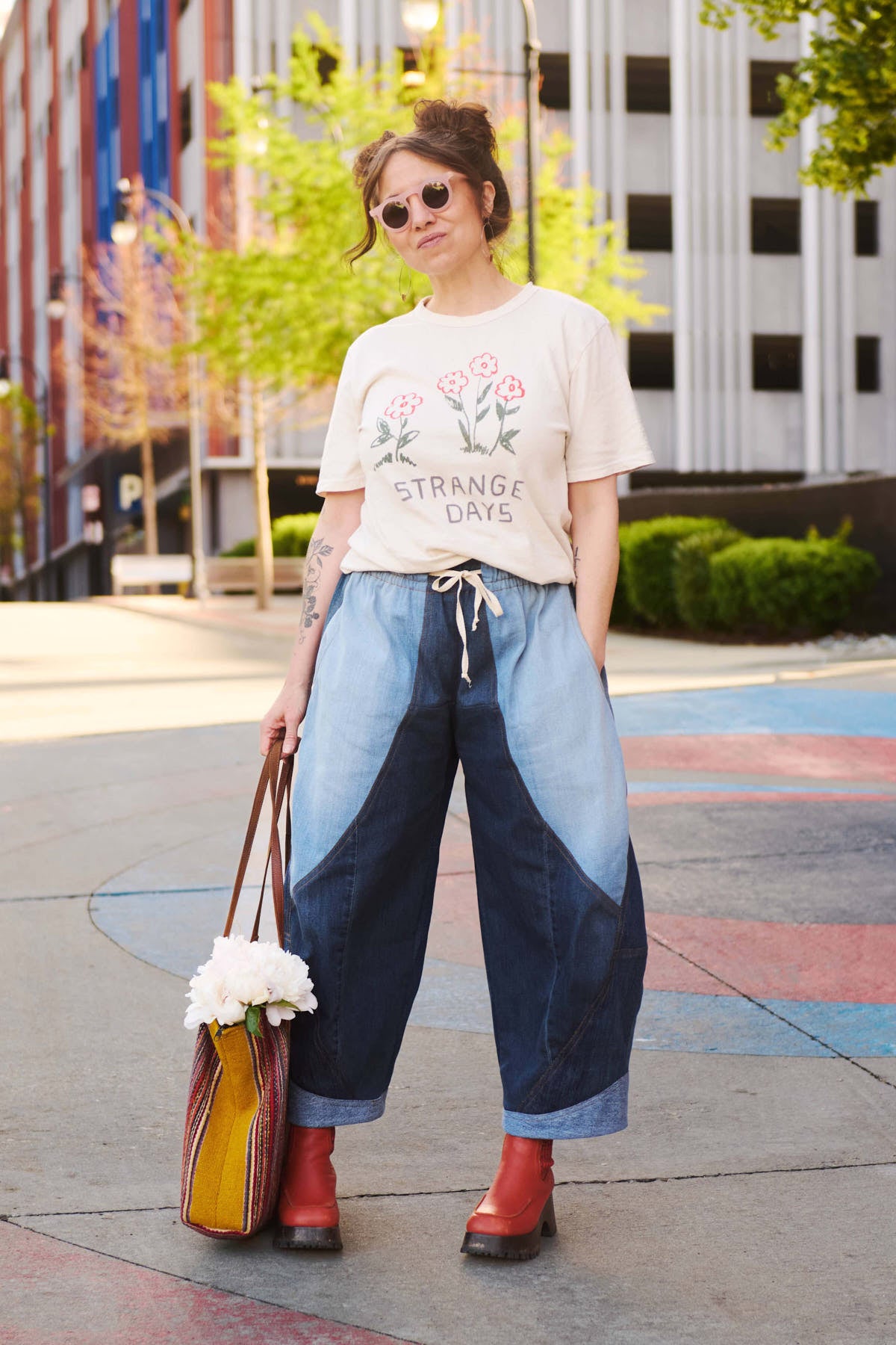 Woman wearing a graphic t-shirt and denim pants with a colorful bag, standing on a city street.